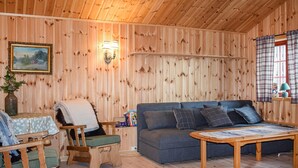 A cozy room with wooden walls, a sofa, a small table, a chair, and a lamp.