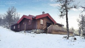 A wooden cabin with a red roof, stone foundation, and a wooden porch.