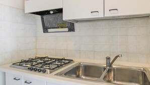 A kitchen with white cabinets, a gas stove, a stainless steel sink, and a ventilation hood. - 3 bedroom awesome apartment in Bibione (Bibione)