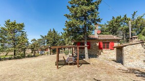 Un bâtiment rustique en pierre, avec des volets rouges, une balançoire en bois et un ciel d’un bleu limpide.