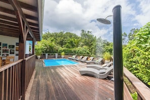 A wooden deck with a pool, lounge chairs, and a water feature. - Villa Kyo - Deshaies, Guadeloupe (Deshaies)
