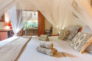 A bedroom with a canopy bed, a sitting area with a chair, and a view of the outdoors. - Villa Kyo - Deshaies, Guadeloupe (Deshaies)
