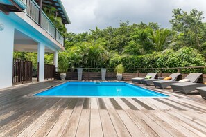 Um deck de madeira com piscina, espreguiçadeiras e vista para vegetação exuberante.