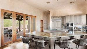 A spacious kitchen with a large island, bar stools, and a sliding glass door leading to an outdoor patio. - ROCKSTAR HOME in DESERT MOUNTAIN - N SCOTTSDALE-PET FRIENDLY-CaveCreek/Carefree (Scottsdale)