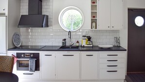 A modern kitchen with white cabinets, a black range hood, a built-in oven, a round window, and a coffee maker. - Cozy apartment in Lagan with WiFi (Lagan)
