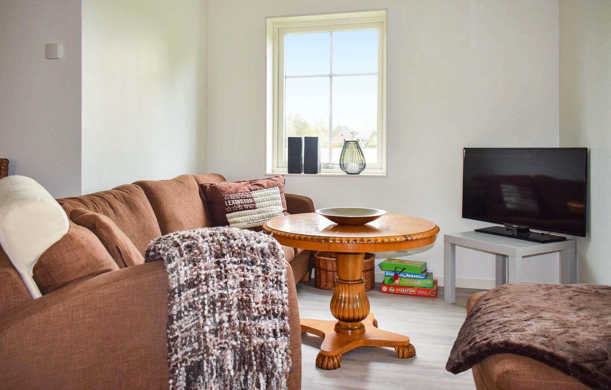 A living room with a brown sofa, a round wooden table, a television, and a window with blinds.