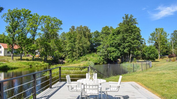 A wooden deck with a table and chairs overlooking a calm river, surrounded by lush greenery and trees. - Cozy apartment in Lagan with WiFi (Lagan)