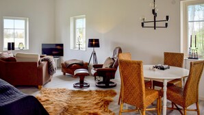 A modern living room with a sofa, armchair, dining table, and chairs. There is a television, a floor lamp, and a chandelier. - Cozy apartment in Lagan with WiFi (Lagan)