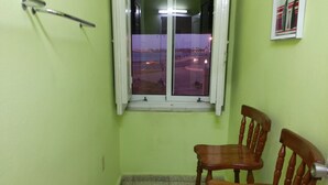 Ein kleiner Raum mit Fenster auf eine belebte Straße im Dämmerlicht, zwei Holzstühle und ein Metallgeländer.