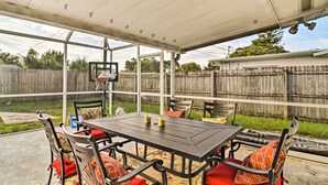 Een overdekt terras met een tafel en stoelen, een basketbalring en een houten omheining op de achtergrond.