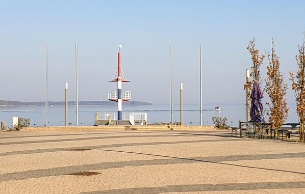 A paved promenade with a tall red and white structure, possibly a lighthouse, and a statue on the right. - Cozy apartment in Rechlin with house sea view (Rechlin)