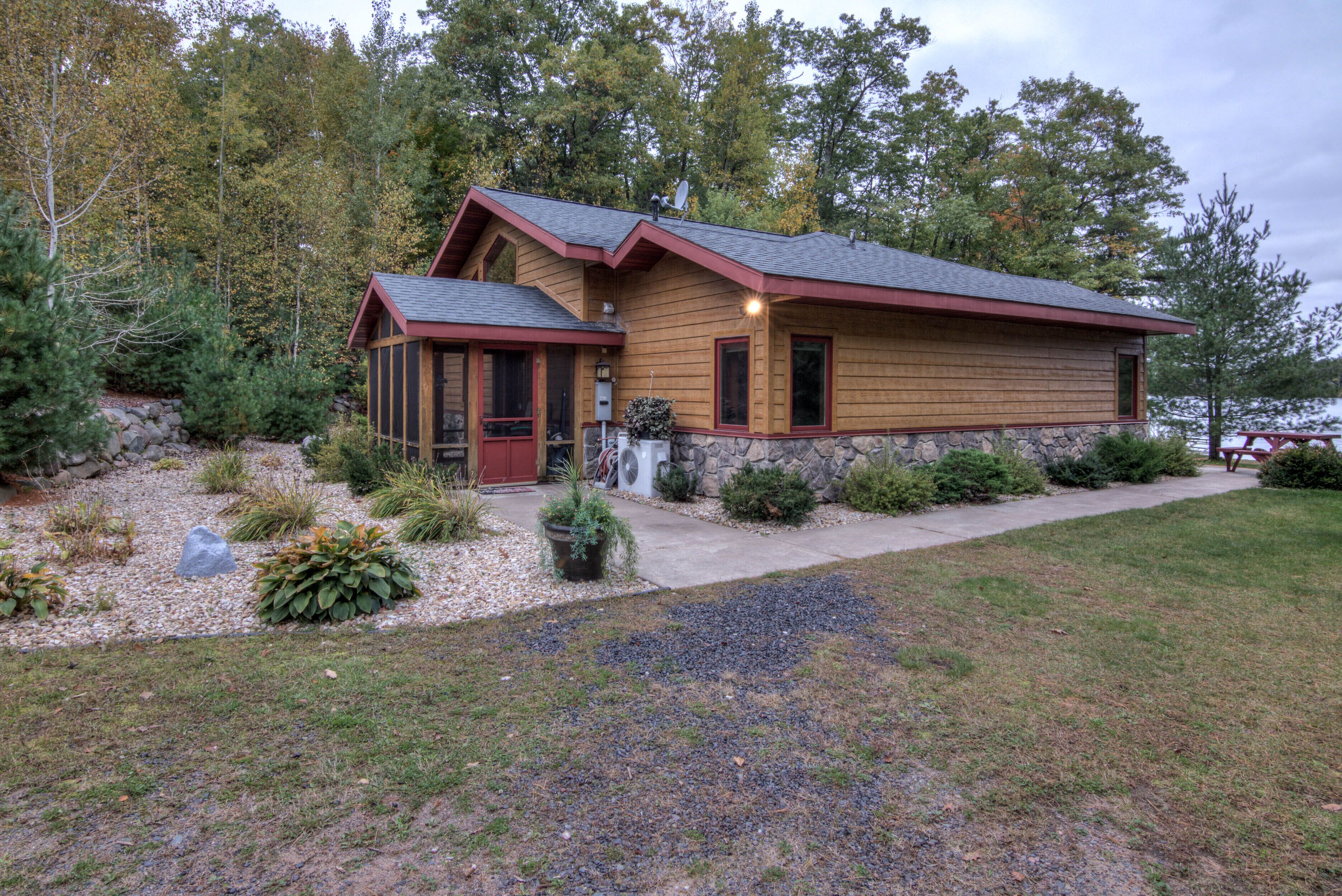 Une cabane en bois avec des fondations en pierre, une porte rouge et une allée gravillonnée.