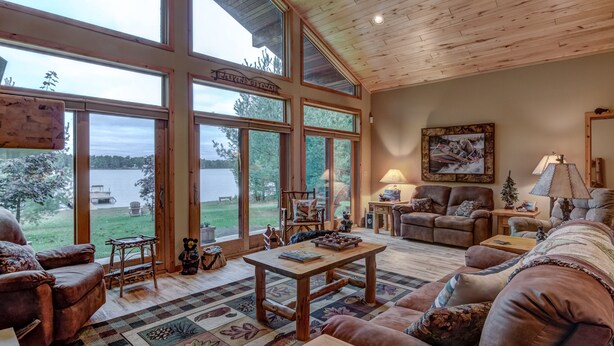 A spacious living room with large windows, a wooden ceiling, and a view of a lake.