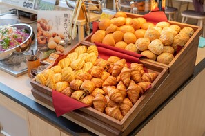 Un bufé con diversas opciones de panadería, incluyendo pan, cruasanes y pasteles.