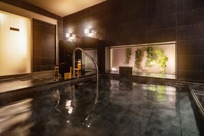 A modern indoor pool with a clear water surface, a seating area with a chair and a small table, and a wall with a green plant display. - Super Hotel Echizen Takefu (Echizen)