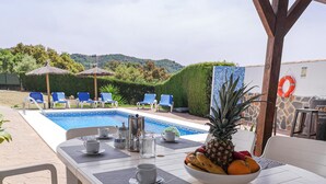 Ein Tisch am Pool mit Frühstücksangeboten, Obstschale und Blick auf Schwimmbecken und Liegestühle.