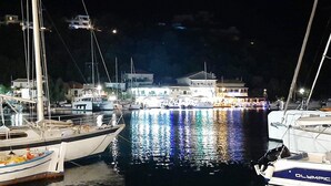 A marina at night with several boats docked, a building with lights in the background, and a clear view of the water reflecting the lights. - Gorgeous home in Lefkada with private swimming pool, can be inside or outside (Lefkada)