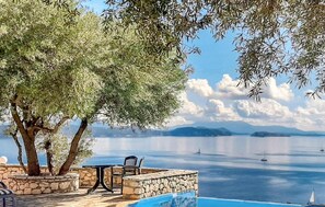 A poolside area with stone walls, outdoor furniture, and a view of the sea with boats. - Gorgeous home in Lefkada with private swimming pool, can be inside or outside (Lefkada)