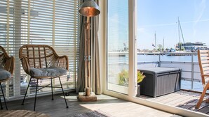 Moderni huone, jossa on suuret ikkunat, rottinkituolit, lattiavalaisin ja näkymä venesatamaan.
