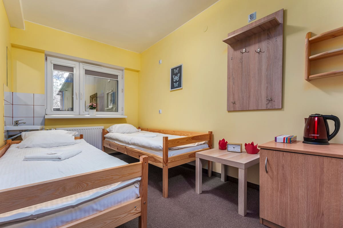Una habitación con tres camas de madera, una mesita, un armario y un ventanal.