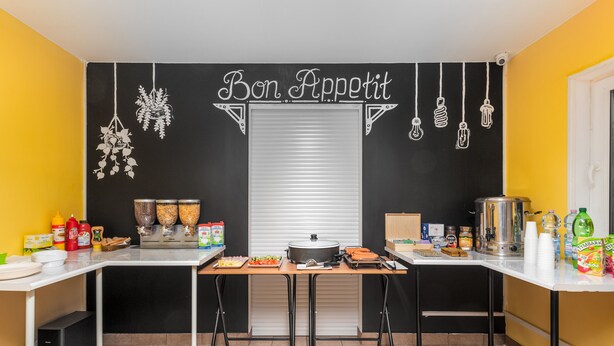 A kitchen with a black and white theme, featuring a 'Bon Appetit' sign, hanging light bulbs, and various kitchen appliances and utensils. - Luxhostel24 Warsaw (Warsaw)