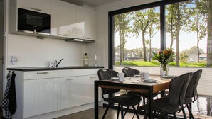 A modern kitchen with white cabinets, a built-in microwave, and a window overlooking a green landscape. - Awesome ship in Well with house sea view (Well)
