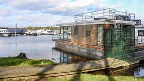 A modern boat house with a wooden deck and metal railings, docked at a marina with several boats. - Awesome ship in Well with house sea view (Well)