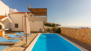 Ein Pool auf dem Dach mit blauen Liegestühlen, einer Pergola und Blick aufs Meer.