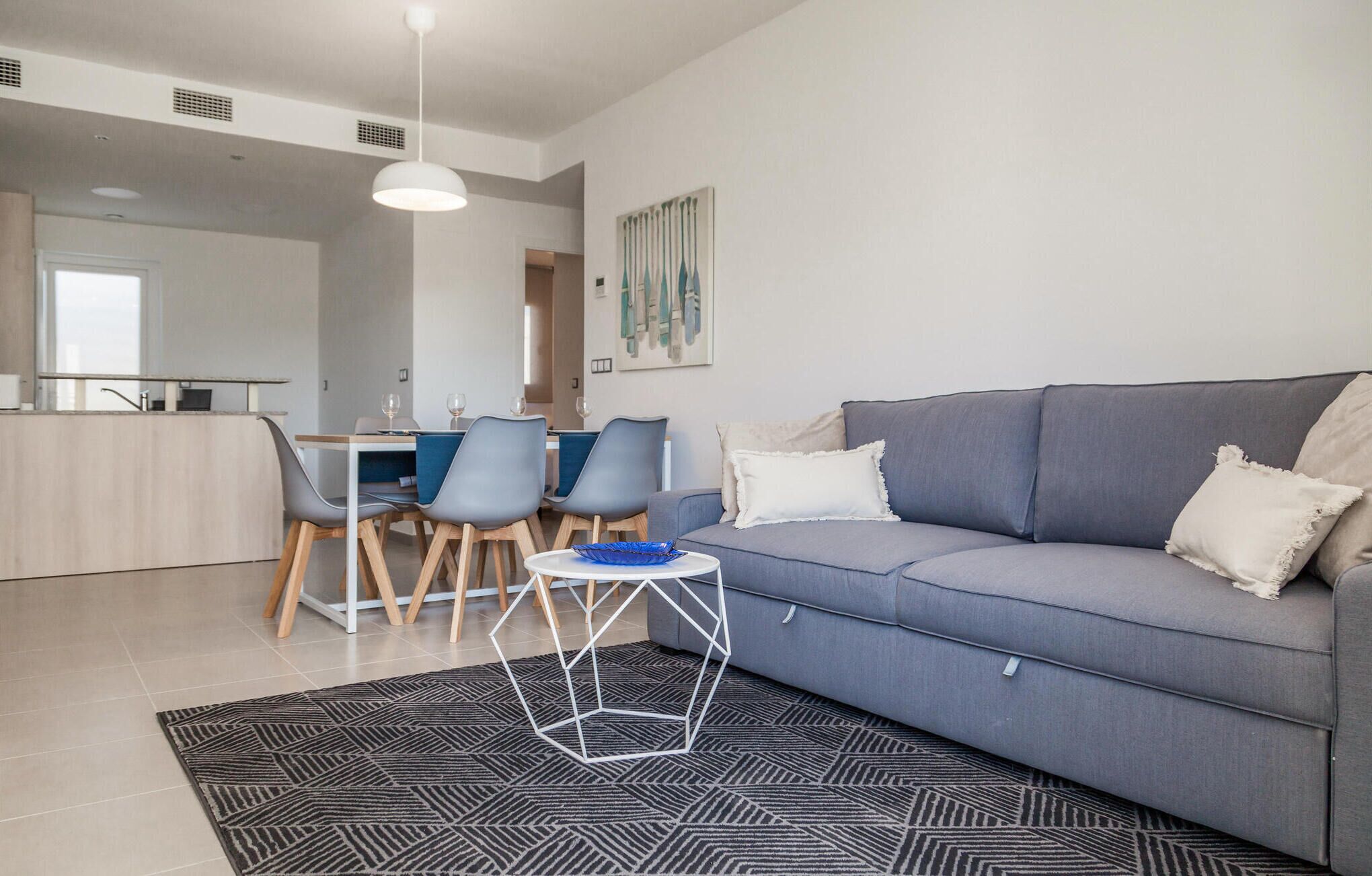 A modern living room with a grey sofa, a coffee table, and a dining area with chairs and a table.