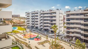 A modern multi-story residential building with balconies, a landscaped courtyard with play equipment, and a clear view of the surrounding area.