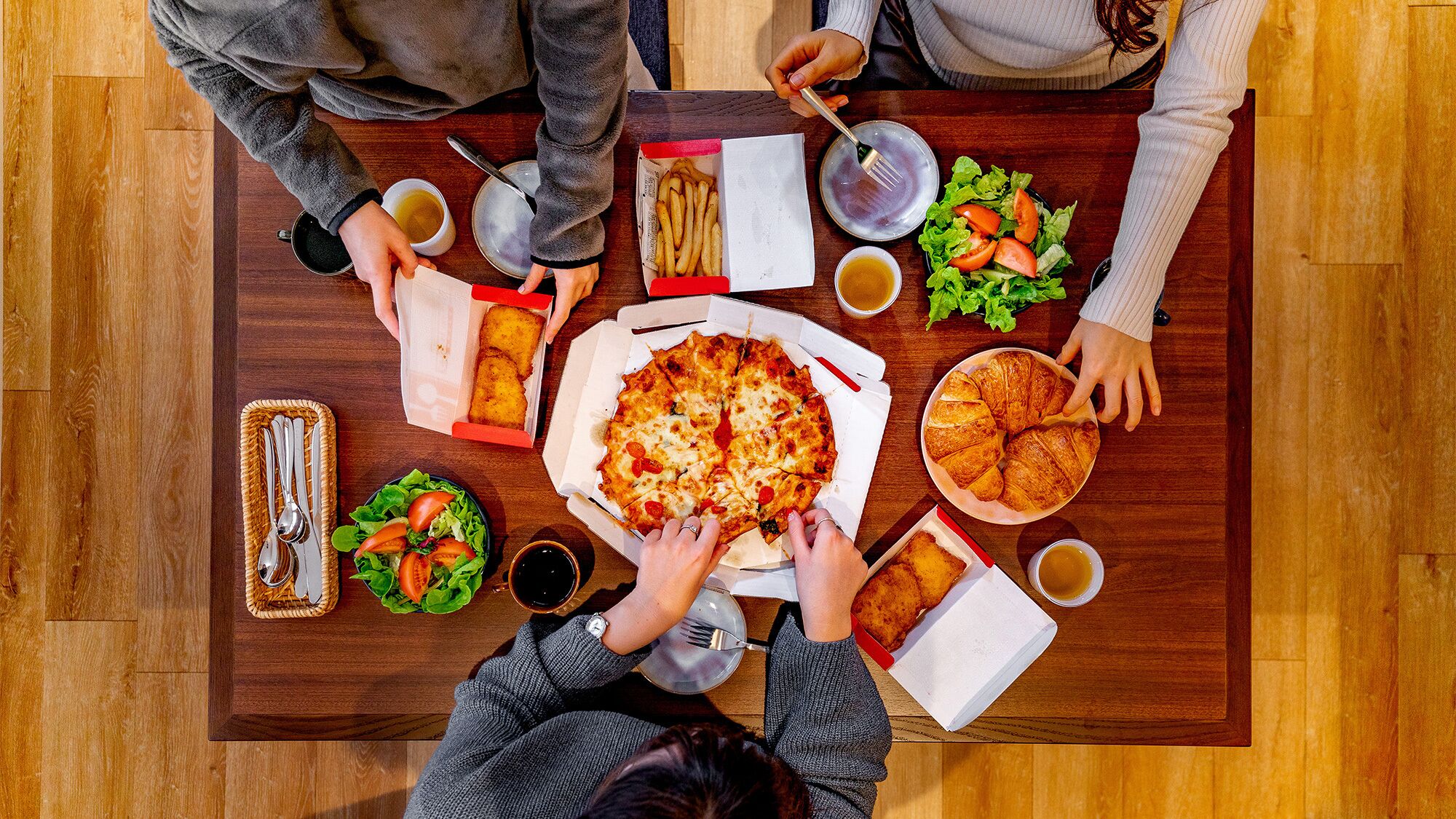 A dining table with a pizza, croissants, fries, salad, and drinks.