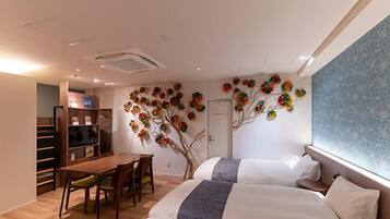 A hotel room with two beds, a dining table with chairs, a small kitchen area, and a decorative wall with a tree design.