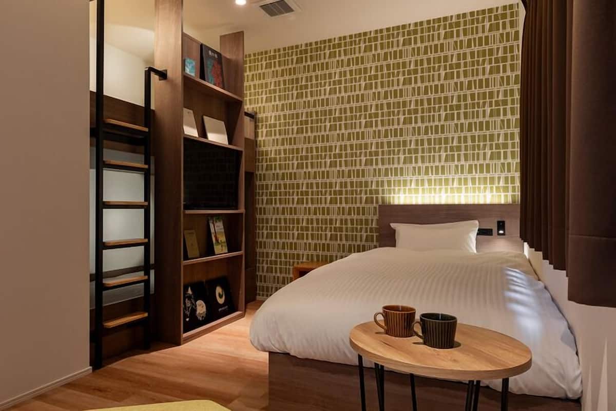Ein Hotelzimmer mit einem Bett, einem Nachttisch aus Holz mit zwei Tassen, einem Bücherregal und einer Wand mit Muster.