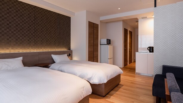 Quarto de hotel com duas camas, uma pequena cozinha e uma área de estar.