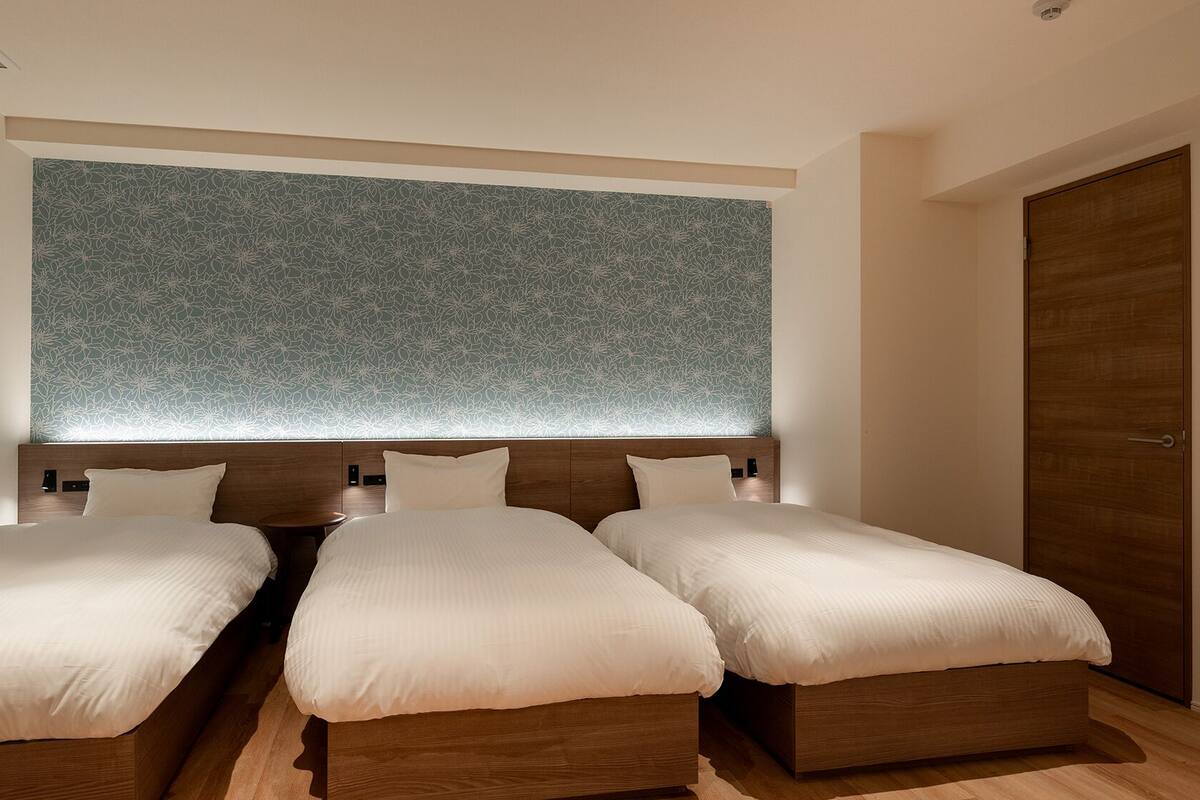 A hotel room with three single beds, a wooden headboard, and a large floral-patterned wall.