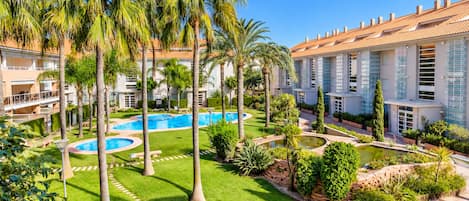 A resort with a central swimming pool, palm trees, and a well-maintained lawn.