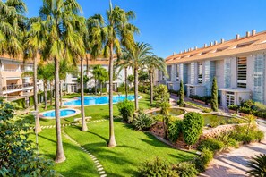 Un resort con piscina central, palmeras y césped bien cuidado.