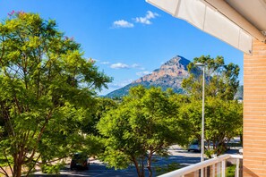 Une vue sur une montagne, avec un ciel dégagé, des arbres au premier plan et un bâtiment à la façade en briques.