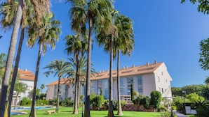 Un hôtel doté d’un grand bâtiment, de palmiers et d’une pelouse bien entretenue.