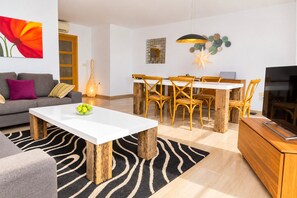 A modern living room with a white coffee table, a sofa, a dining area with wooden chairs, a TV, and a decorative star hanging from the ceiling. - Golden Gardens Duplex Apartment Javea Arenal s, 3 Terraces, AACC, Wifi and only 600m from the Beach (Javea / Xàbia)