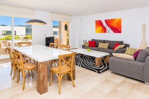 A modern living room with a dining area, a grey sofa with colorful cushions, and a large abstract painting on the wall. - Golden Gardens Duplex Apartment Javea Arenal s, 3 Terraces, AACC, Wifi and only 600m from the Beach (Javea / Xàbia)