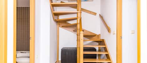 Una escalera en espiral de madera en una habitación con un muro de azulejos y un cuadro.