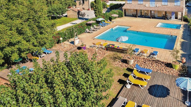 A large outdoor swimming pool with multiple sun loungers and umbrellas, surrounded by lush greenery and a stone pathway.
