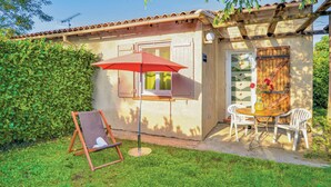 A small house with a patio, a wooden table with two chairs, a red umbrella, and a wooden swing chair.