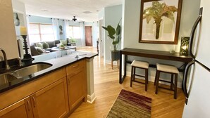 A modern kitchen with wooden cabinets, a black countertop, and a built-in island. There is a dining area with a table and two chairs. - The Tropical Bungalow (Safety Harbor)