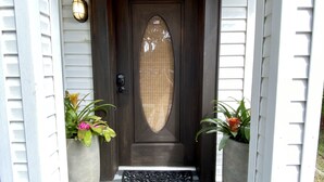 A dark brown front door with the number 124, flanked by two large potted plants, and a black doormat. - The Tropical Bungalow (Safety Harbor)