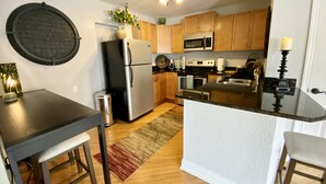 A compact kitchen with wooden cabinets, a stainless steel refrigerator, a microwave, and a stove. - The Tropical Bungalow (Safety Harbor)