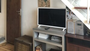 Huoneessa on portaikko, jalustalla oleva televisio, ovi ja hylly, jossa on erilaisia esineitä.