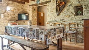 Ein rustikaler Essbereich mit Holztisch, bedeckt mit einer gemusterten Tischdecke, Steinwänden und einem Steinkamin mit einer Uhr.