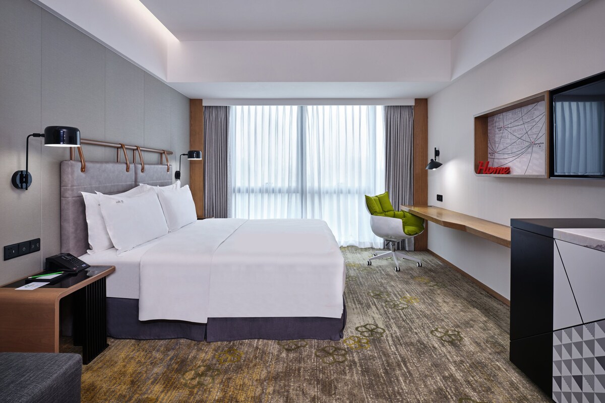 A modern hotel room with a large bed, a desk, a chair, and a television.
